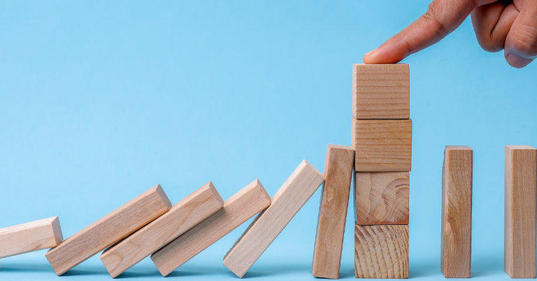 A hand stabilizing wooden dominoes to prevent them from falling
